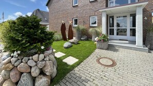 A modern brick house with a well-maintained garden, stone pathway, and a front door with glass panels. - Strandvilla Wohnung Strand-loft (Sylt)