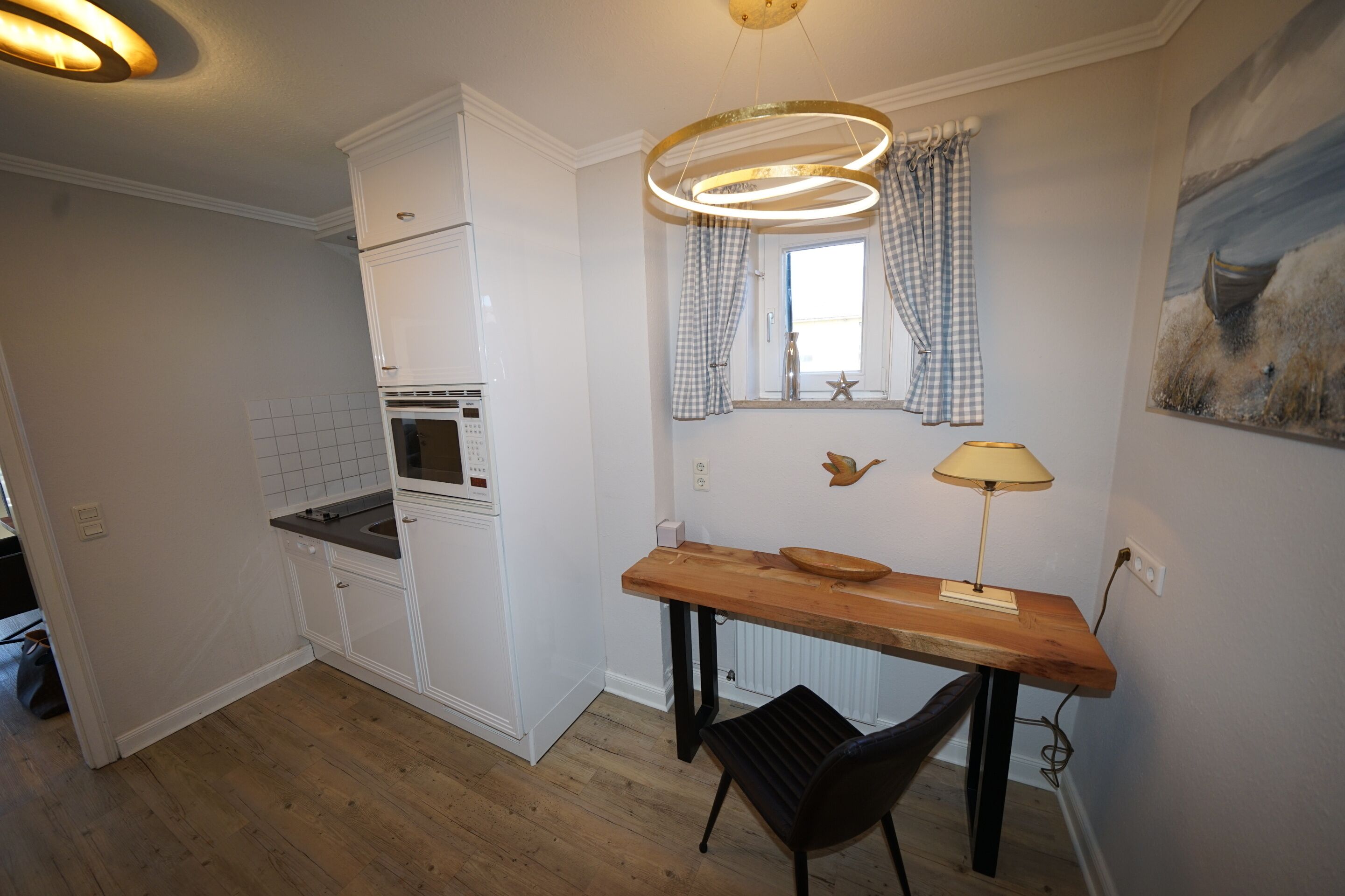 A compact kitchen with white cabinets, a wooden countertop, a black chair, and a pendant light.