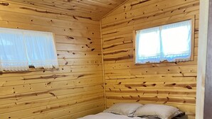 Een houten kamer met een bed, twee ramen met kantgordijnen en een deur met een bloemenmotief.