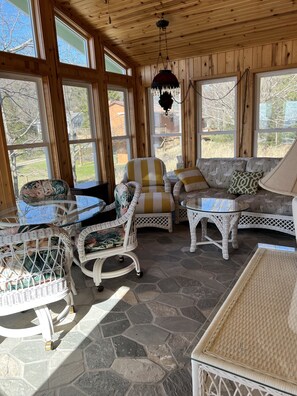 Relax in a spacious room with a sofa, chairs, and a wicker chair, surrounded by large windows and a rustic ceiling.