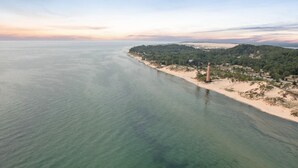 Luchtbeeld van een kustgebied met een vuurtoren, zandstrand en weelderige begroeiing.
