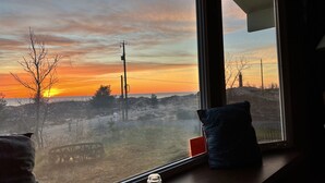 Ett rum med utsikt över en strand vid solnedgången, en fönsterbräda med en flaska och en kudde.