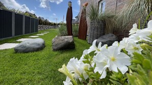 Ein gepflegter Garten mit einem Backsteinhaus, großen Steinen und weißen Blüten.