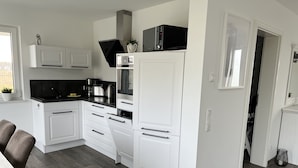 A modern kitchen with white cabinetry, a black countertop, and a stainless steel range hood. - Vacation home Hilde on the lake with private beach for 4 adults, fireplace, boat and sauna (Löbnitz)