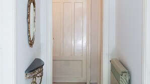 Un pasillo con una puerta blanca, un radiador y un espejo fijado a la pared.
