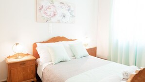 Una cama bien hecha con un cabecero de madera, dos mesitas de noche con lámparas y una obra de arte floral en la pared.