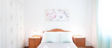A hotel room with a wooden bed, two bedside tables with lamps, a floral artwork on the wall, and a patterned floor.