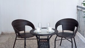 Una mesa redonda de cristal con dos sillas de mimbre, cada una con una taza y un termo encima.