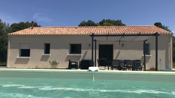 Un bâtiment doté d’un toit en tuiles, d’une piscine et d’un espace extérieur aménagé pour s’asseoir.