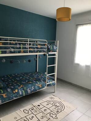 Un lit superposé avec un matelas à motifs de jungle, une échelle en métal blanche et une lampe suspendue.