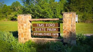Ein Steinschild mit der Aufschrift "TIMS FORD STATE PARK GRÜNDUNG 1978" in einer natürlichen Umgebung.