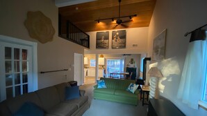 A spacious living room with a high ceiling, a green sofa, a beige couch, and a black entertainment unit. - Peaceful Cottage on Lake Michigan (Two Rivers)