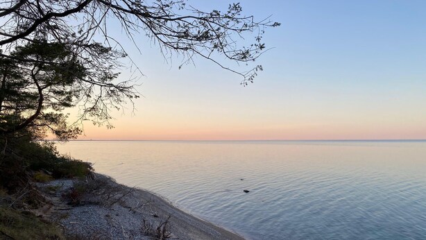A coastal landscape with a pebbly beach, calm sea, and sparse vegetation. - Peaceful Cottage on Lake Michigan (Two Rivers)