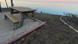 A wooden picnic table with benches, set on a sandy area with a view of the water. - Peaceful Cottage on Lake Michigan (Two Rivers)