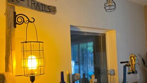 A room with a wooden sign indicating 'Beach' and 'Trails' directions, a hanging light fixture, and a wooden table with wine bottles and glasses. - Peaceful Cottage on Lake Michigan (Two Rivers)