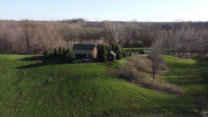 A cabin surrounded by a forest, with a small pond and a grassy field in the foreground. - Countryside Cabin on 40 Private Acres Along Johnson Creek (Lyndonville)