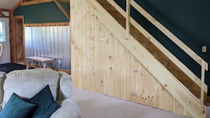 A room with a wooden staircase, a green wall, and a beige sofa with pillows. - Countryside Cabin on 40 Private Acres Along Johnson Creek (Lyndonville)