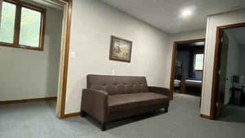 A room with a brown sofa, an exit sign, a framed picture on the wall, and a window.