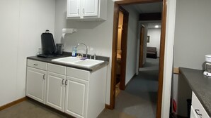 A kitchen with white cabinets, a sink, and a countertop. There is a door leading to another room. - Outlaw Lodge (McCoy Floor 2nd)ATV,SXS, MX Offroad lodging (Iaeger)