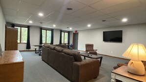 A spacious room with a large brown sofa, a wooden table, a lamp, and a flat-screen TV mounted on the wall. - Outlaw Lodge (McCoy Floor 2nd)ATV,SXS, MX Offroad lodging (Iaeger)