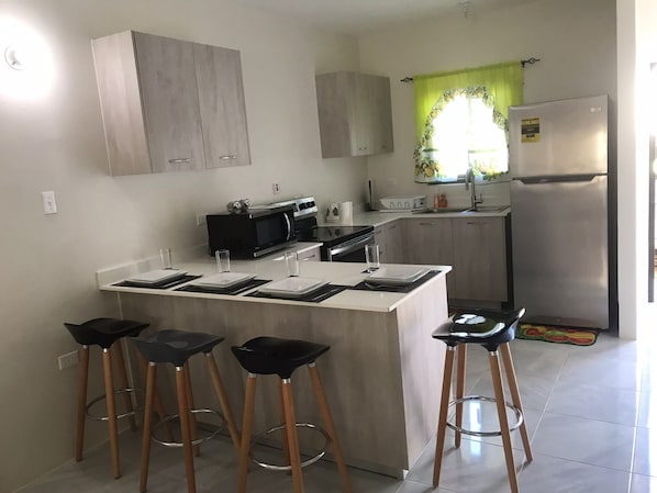 A modern kitchen with a central island, bar stools, a refrigerator, and a microwave.