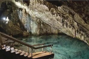 A cave with a clear pool and a staircase leading down.