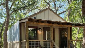 A wooden cabin with a porch and a staircase leading to a deck. - #13 Son's Geronimo - Birdhouse Cabin (Seguin)