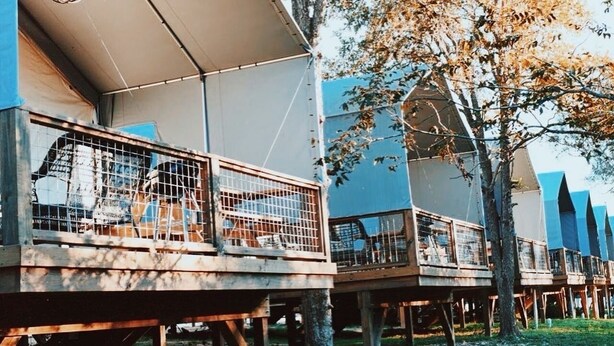A row of treehouse-style cabins with wooden decks and metal railings, connected by a covered walkway. - #13 Son's Geronimo - Birdhouse Cabin (Seguin)