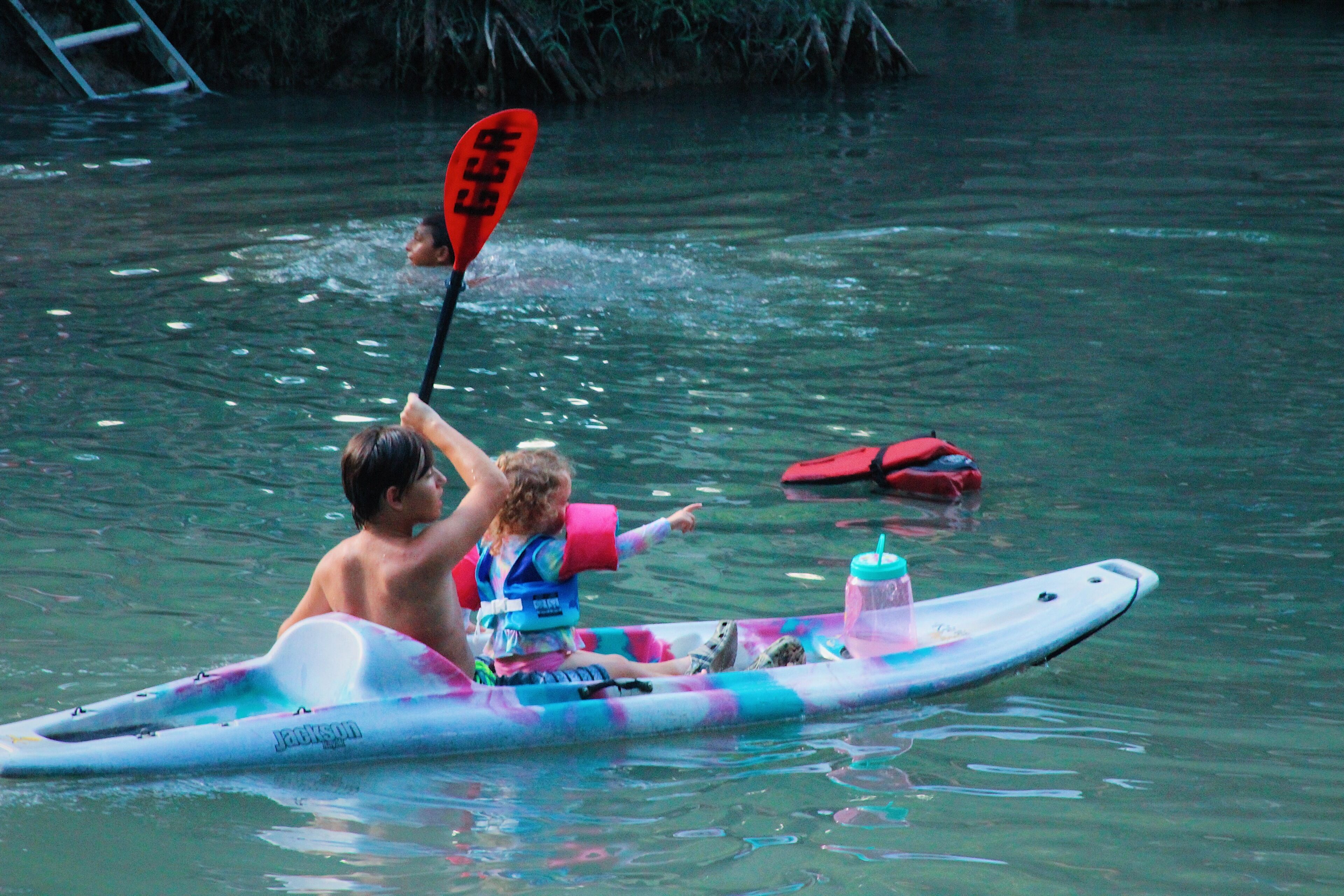 Ein Mann und ein Kind auf einem bunten Stand-Up-Paddle-Board auf dem Wasser.