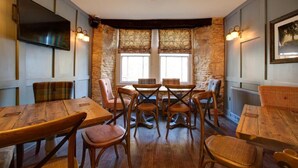 A dining area with wooden tables and chairs, stone walls, and a television mounted on the wall. - The Temple Inn (Bristol)