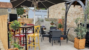 An outdoor patio with tables and chairs, surrounded by stone walls and potted plants. - The Temple Inn (Bristol)