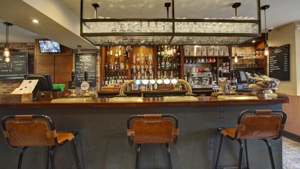 A bar area with a counter, stools, and a variety of bottles and glasses. - The Temple Inn (Bristol)