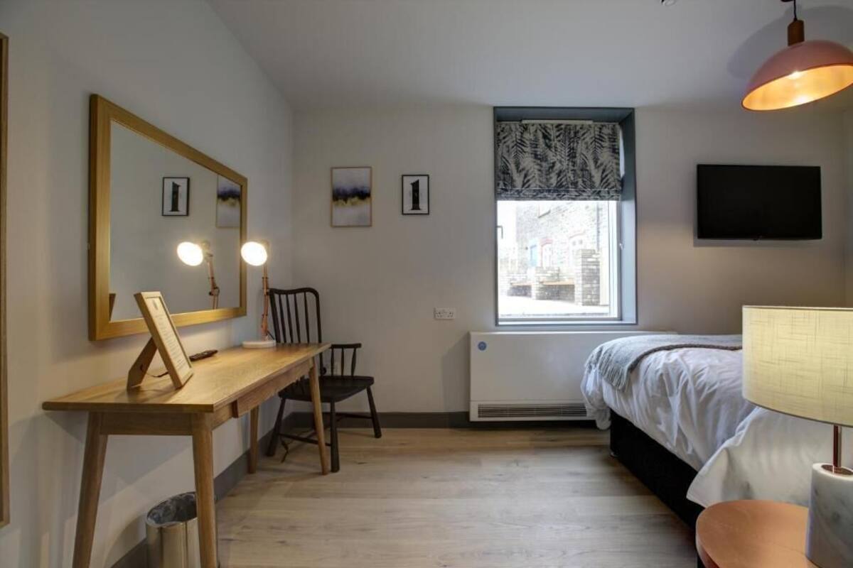 A bedroom with a bed, a desk with a mirror, a chair, a window with a view, and a TV on the wall.