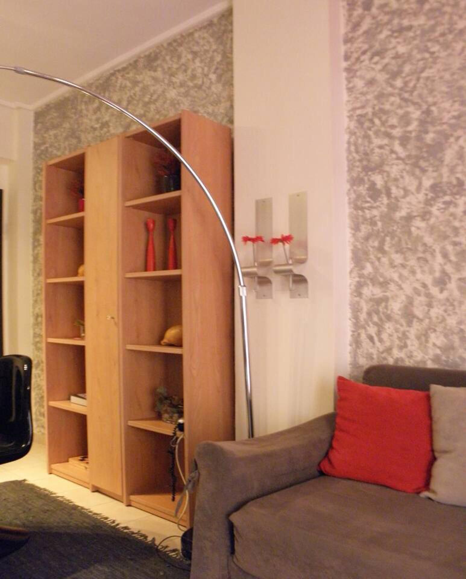 A living room with a wooden bookshelf, a grey sofa with red cushions, and a floor lamp.