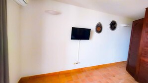 Ein Zimmer mit Flachbildfernseher an der Wand, einer Holztür und einem gefliesten Boden.