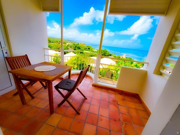 A balcony with a wooden table and chairs, a view of the ocean, and a tiled floor.
