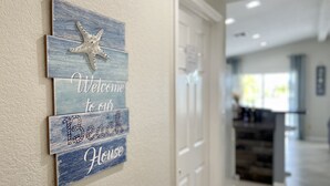 Un couloir avec une pancarte d’accueil représentant une étoile de mer et les mots « Bienvenue dans notre maison de vacances au bord de la plage ».