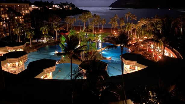 Un complex turístic amb diverses piscines, palmeres i vista a l'oceà de nit.