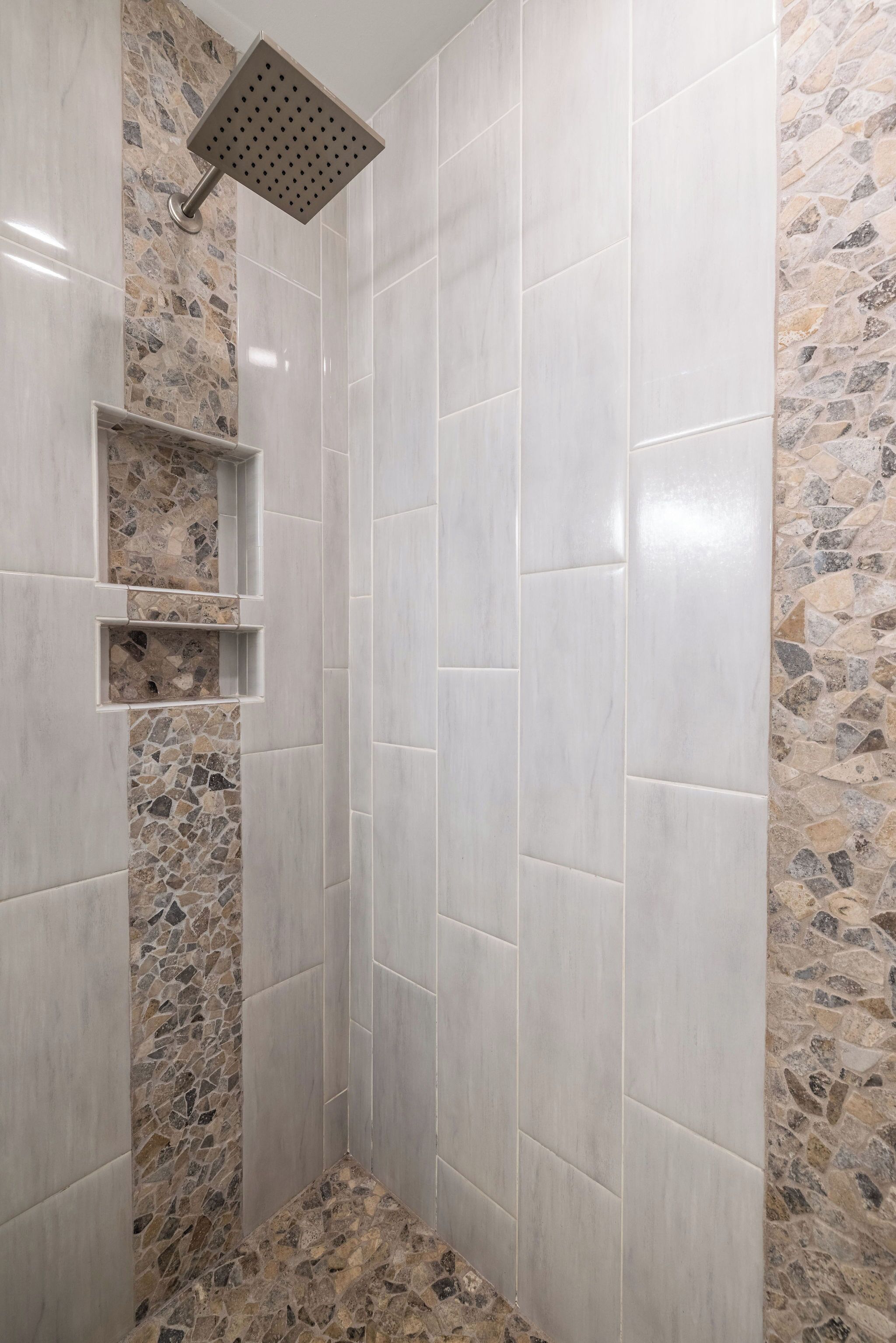 A shower with a square showerhead, tiled walls, and a stone accent wall.