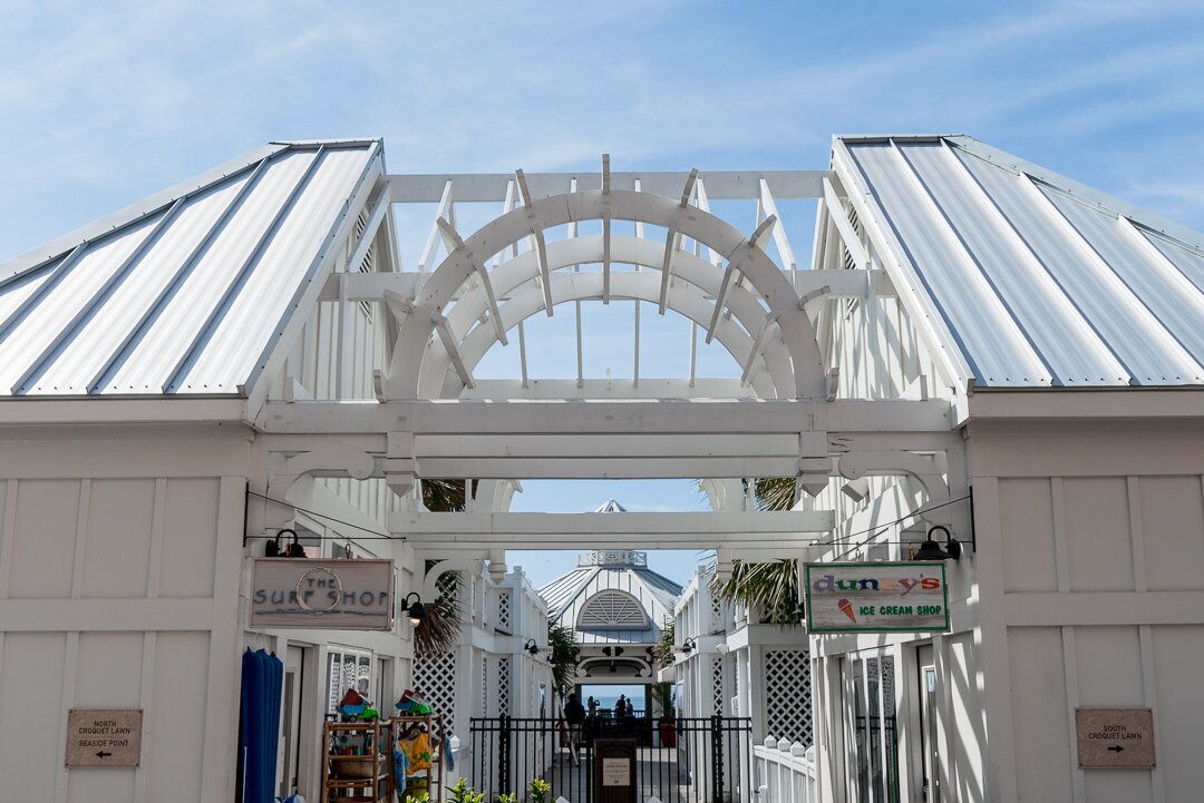 Un arco de metal blanco con letreros que indican 'The Surf Shop' y 'Dun's Ice Cream Shop'.