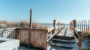 Een houten looppad dat naar een strand leidt, met aan één kant een houten hek en aan de andere kant een metalen lantaarnpaal.