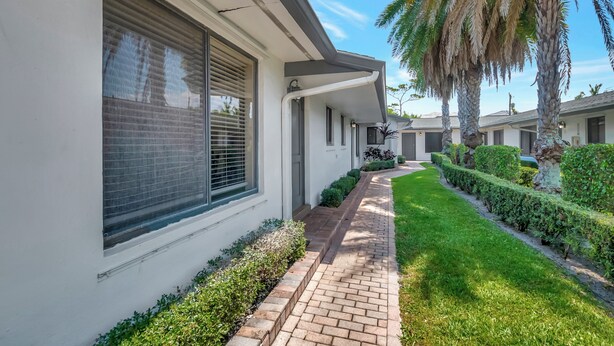 A residential building with a brick pathway, neatly trimmed hedges, and palm trees. - Spacious and Bright 2bed, washer/dryer, back yard (Delray Beach)