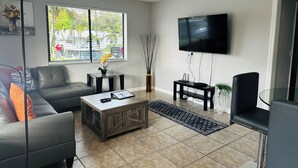 A living room with a sofa, coffee table, TV, and a window with blinds. - Spacious and Bright 2bed, washer/dryer, back yard (Delray Beach)