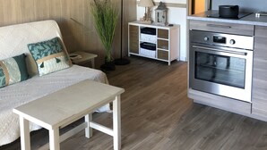Una cocina moderna con horno empotrado, suelo de madera y una zona de comedor con banco y mesa.