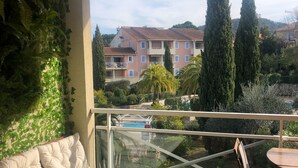 Un balcón con sofá y una mesa de madera, con vista a una piscina y un edificio con varios balcones.