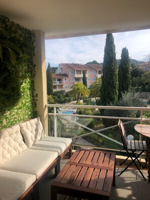 Un balcone con un divano e un tavolo di legno, con vista su una piscina e un edificio con numerosi balconi.