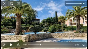 Zona piscina con palme e pareti in pietra, immersa nel verde e circondata da edifici.