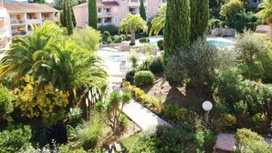 Un resort con piscina rodeada de abundante vegetación, incluyendo palmeras y cipreses. Se observan varias edificaciones con balcones y una vista despejada del área de la piscina.