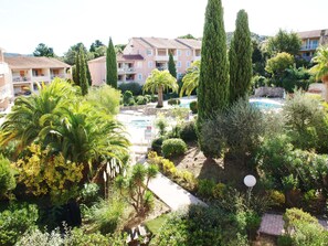 Un resort con piscina circondata da vegetazione lussureggiante, tra cui palme e cipressi. Si vedono diversi edifici con balconi e una vista libera sulla zona della piscina.