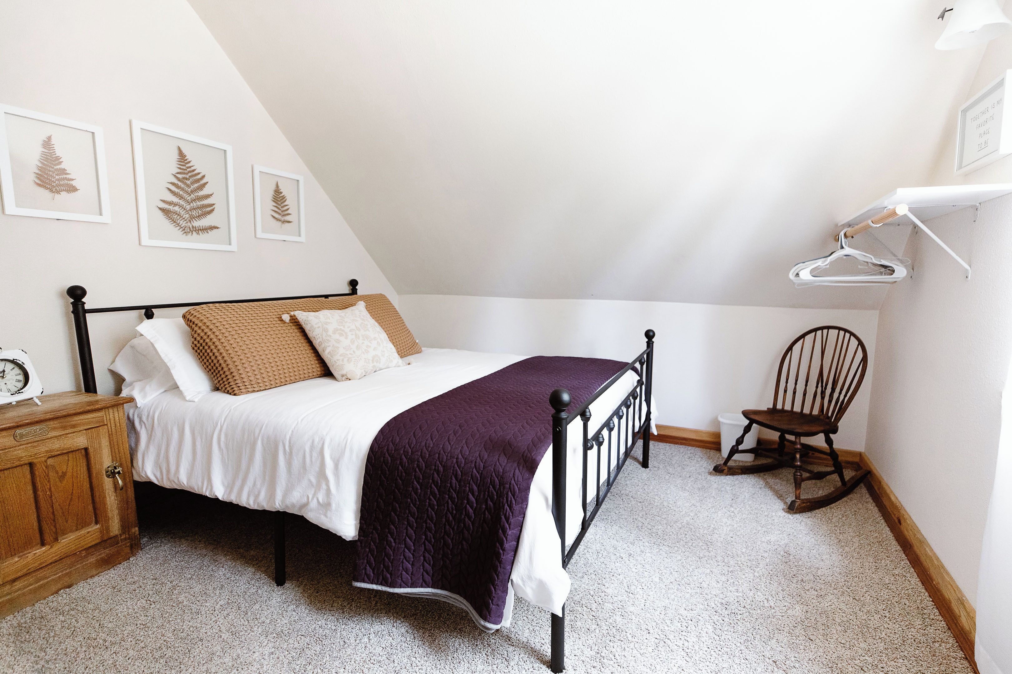 A bedroom with a bed, a wooden dresser, a rocking chair, and framed leaf art on the wall.